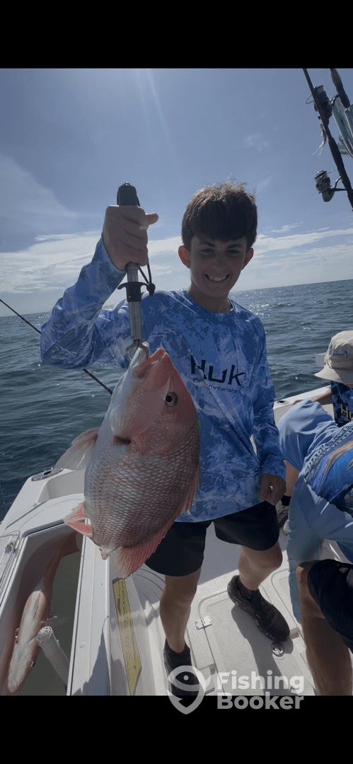 A young angler proudly displaying a large Snapper while fishing on a boat, showcasing a successful day on the water.