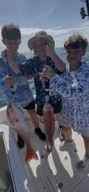 Three young anglers proudly displaying their catch of Red Snapper while fishing on a boat.