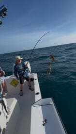 A young angler is reeling in multiple fish while fishing on a boat, showcasing an exciting catch in the open water.
