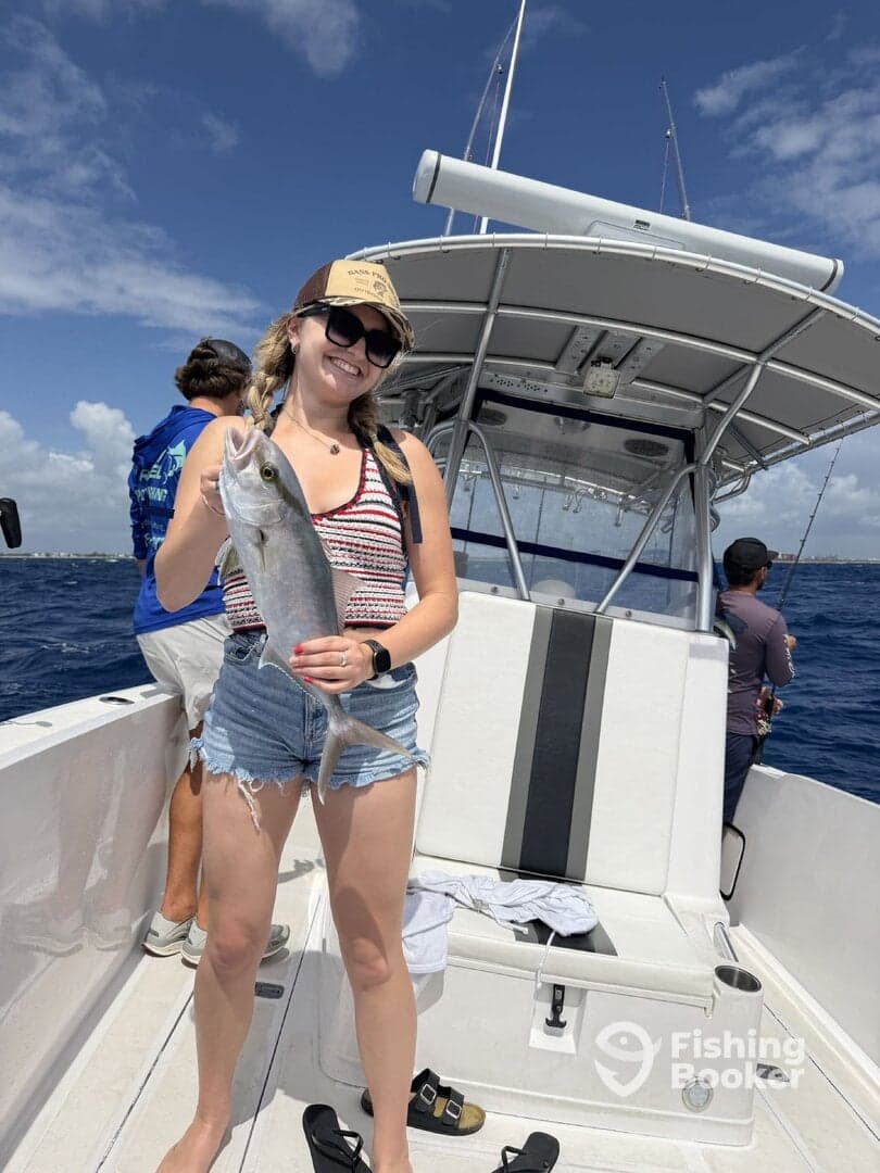 A young woman proudly displaying her catch, a large fish, while aboard a fishing boat in sunny waters.