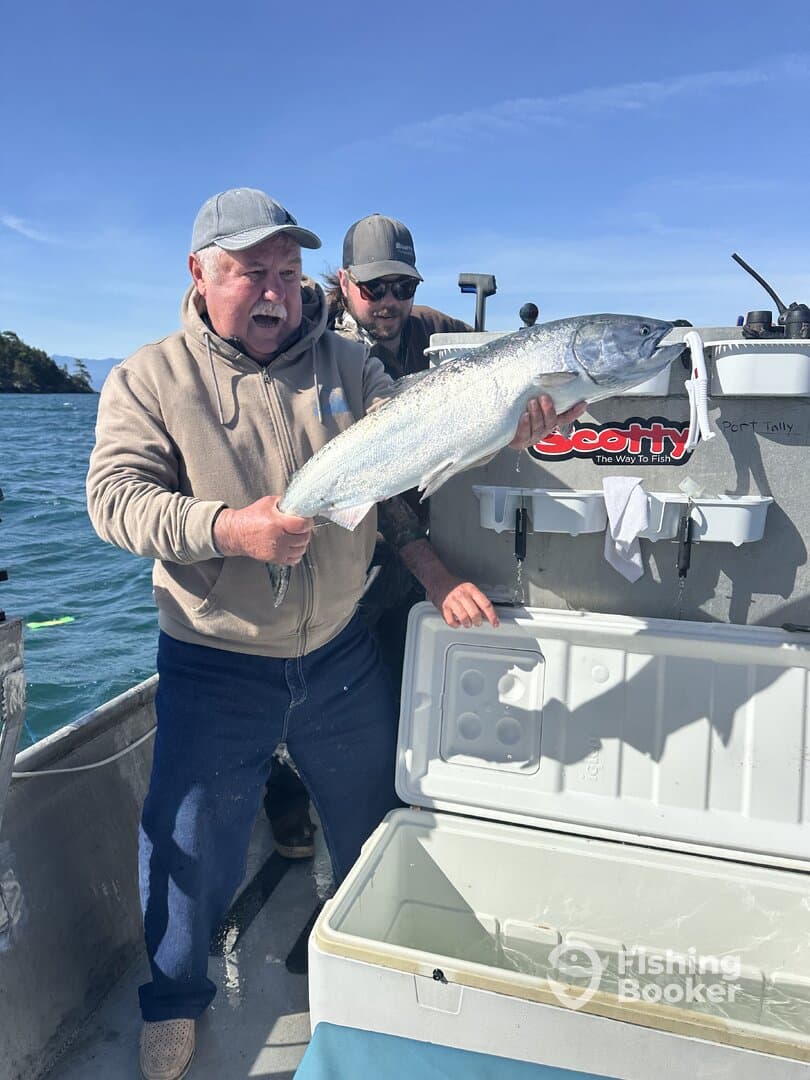 An excited angler proudly displaying a large salmon on a fishing boat, showcasing a successful day on the water.