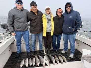 A group of anglers proudly displaying their catch of several Speckled Trout on a foggy day out on the water.