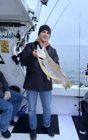 A young angler proudly displaying a large Brown Trout while fishing on a charter boat.