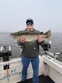 A young angler proudly displaying a large Speckled Trout while fishing on a boat in foggy conditions.