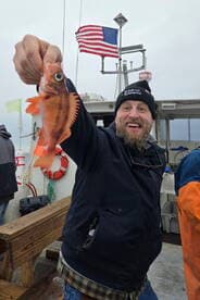 A happy angler proudly displaying a vibrant Rockfish on a fishing charter, with the American flag waving in the background.