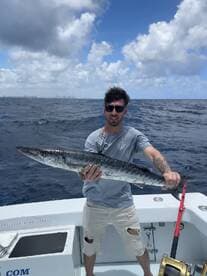 Angler proudly displaying a large King Mackerel while fishing offshore, with a scenic ocean backdrop.