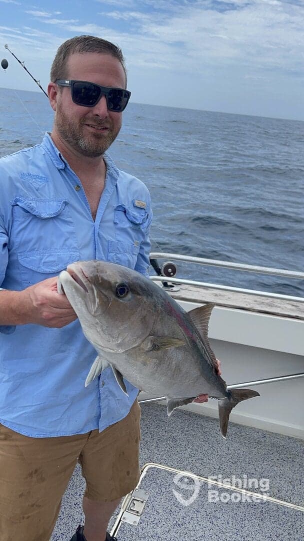 Angler proudly displaying a large Amberjack while fishing offshore, showcasing a successful day on the water.