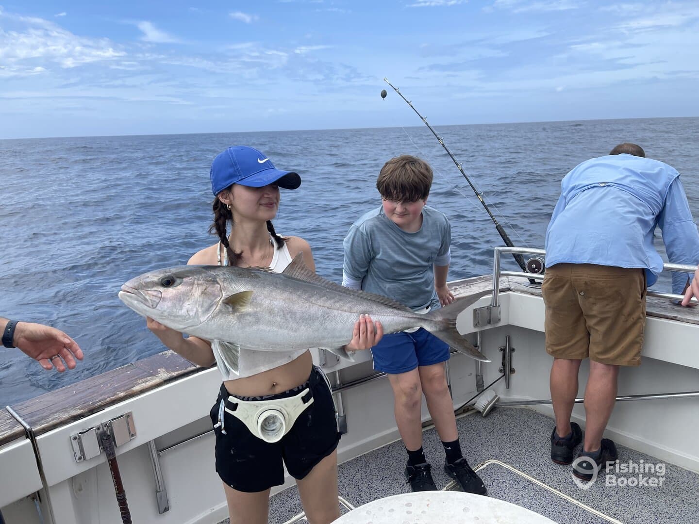 A young angler proudly displaying a large fish while fishing with friends on a boat in open water.