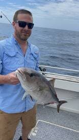 Angler proudly displaying a large Amberjack while fishing offshore, showcasing a successful day on the water.