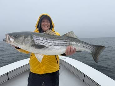 Angler proudly displaying a large Striped Bass while fishing on a cloudy day.