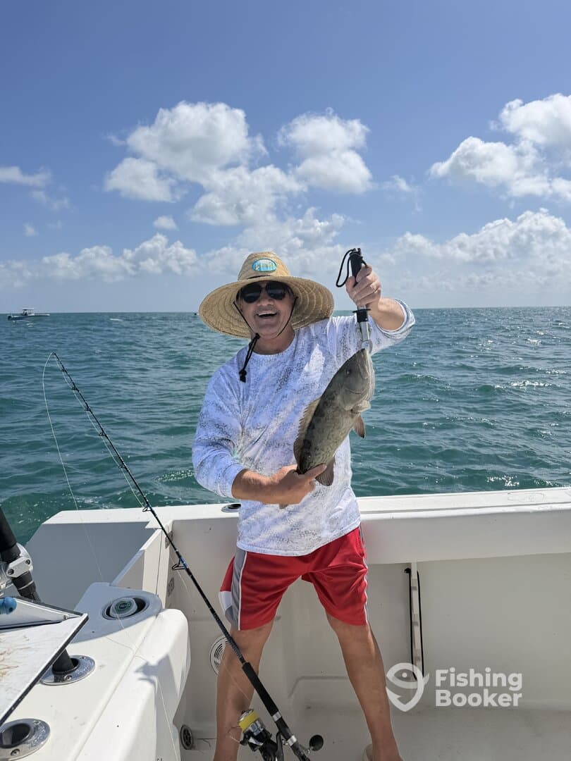 An enthusiastic angler proudly displaying a large fish while fishing on a boat in sunny waters.