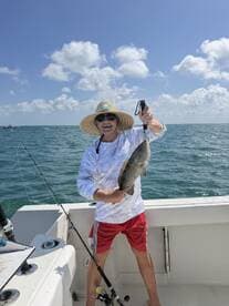 An enthusiastic angler proudly displaying a large fish while fishing on a boat in sunny waters.