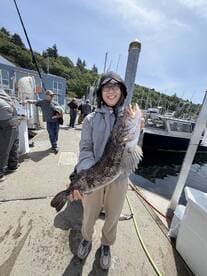 A proud angler holding a large Lingcod at the dock, showcasing a successful fishing trip.