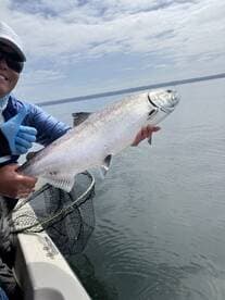 Angler proudly displaying a large Salmon while fishing on a calm lake, showcasing a successful catch.
