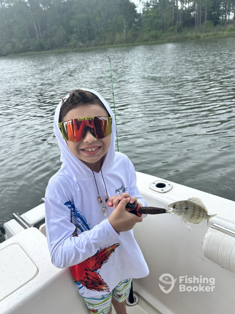 Young angler proudly holding a small fish while fishing on a boat in a serene lake setting.