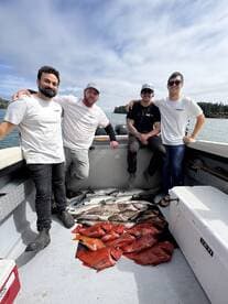 A group of four anglers proudly displaying their catch of vibrant Red Snapper and other fish aboard a fishing boat in a scenic coastal environment.