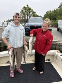 Two anglers proudly displaying their catch of striped bass on a boat after a successful fishing trip.