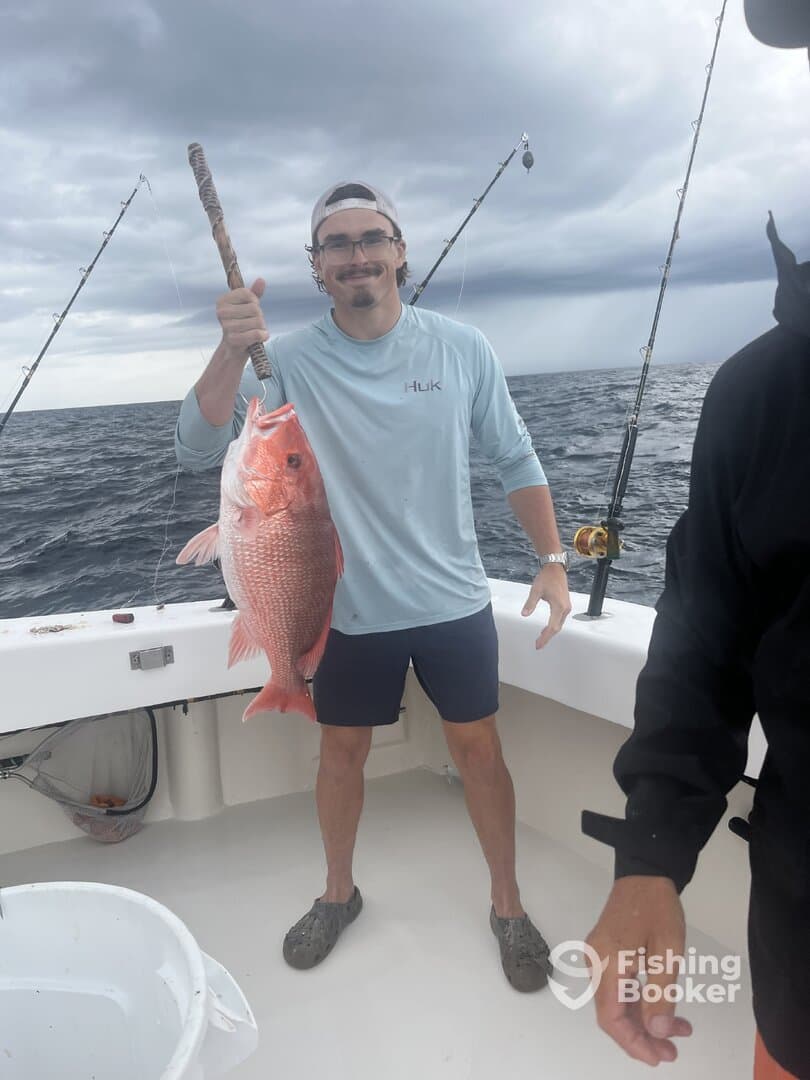 Angler proudly displaying a large Red Snapper while fishing offshore, with stormy skies in the background.