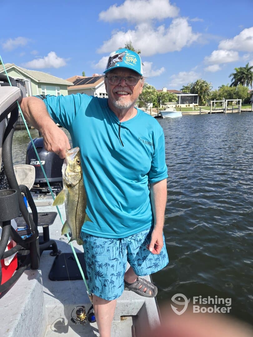 An angler proudly displaying a Snook caught while fishing from a boat in a scenic waterway.