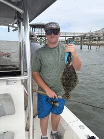 Young angler proudly holding a Flounder while fishing from a boat, showcasing a successful catch during a coastal fishing trip.