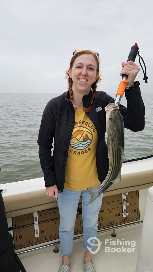 Angler proudly displaying a striped bass while fishing on a boat, showcasing a successful day on the water.