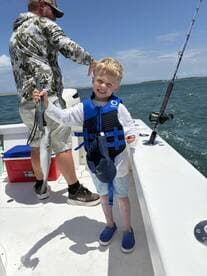 A young angler proudly displaying a caught fish while wearing a life jacket on a fishing boat.