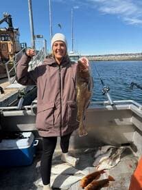 A proud angler holding a large fish on a boat, showcasing a successful fishing trip with multiple fish laid out on the deck.