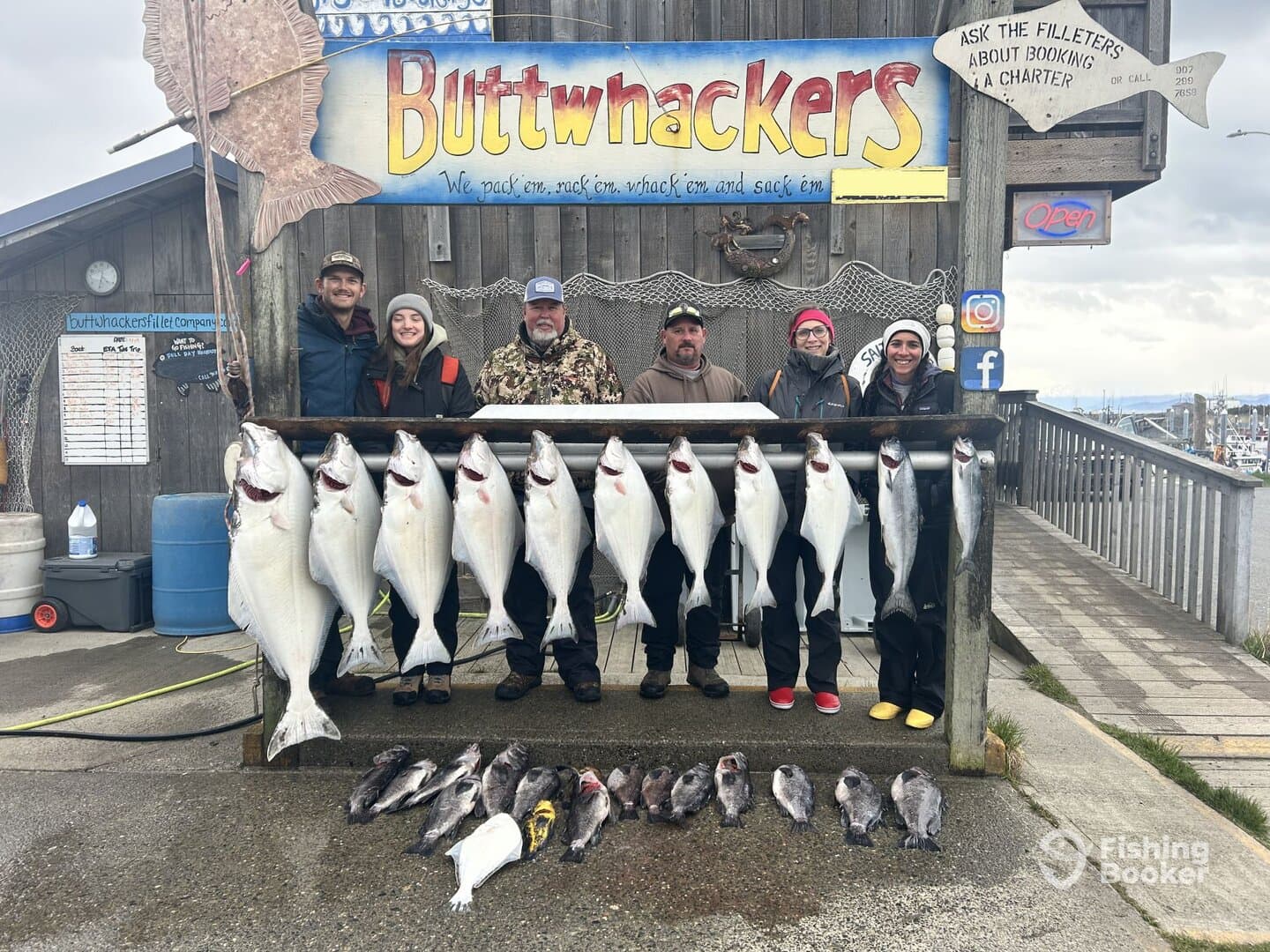A group of anglers proudly displaying their catch of halibut and rockfish on a catch board at the dock, showcasing a successful fishing trip.