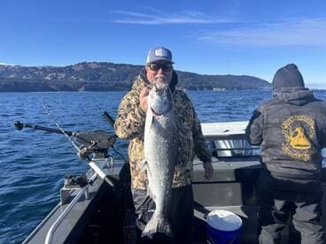 Angler proudly displaying a large salmon while fishing on a boat in a scenic coastal environment.