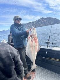 Angler proudly displaying a large Halibut on a fishing charter in a scenic coastal environment.
