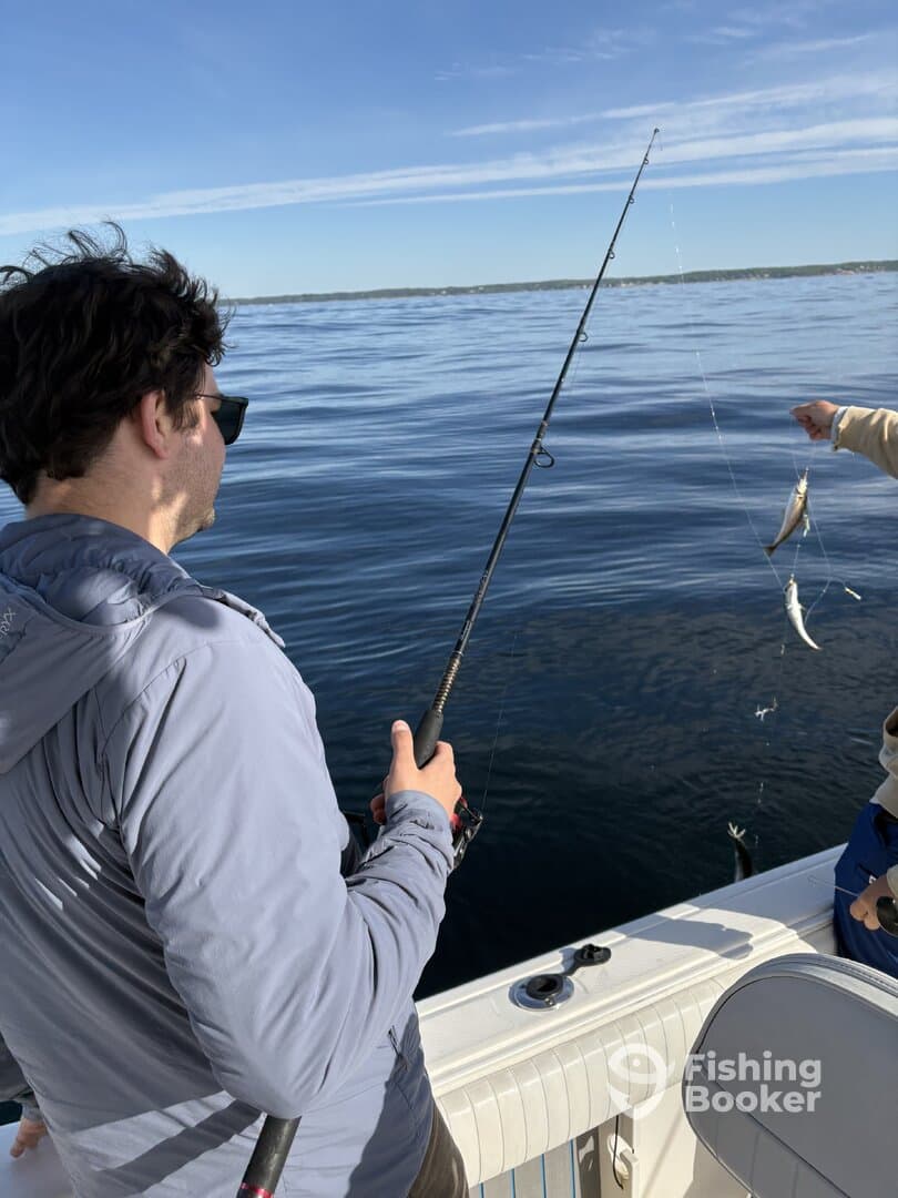 An angler casting a line while another person prepares to reel in a catch on a calm day at sea.