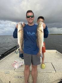 A proud angler and a young boy display their catch of two Redfish while fishing on a boat.