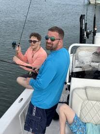 A father and son duo enjoying a fishing trip on a boat, with the son actively reeling in a catch while the younger sibling relaxes nearby.