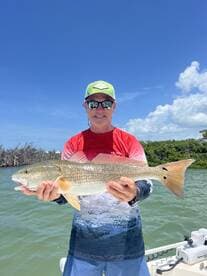 Angler proudly displaying a Redfish while fishing on a sunny day in a coastal environment.