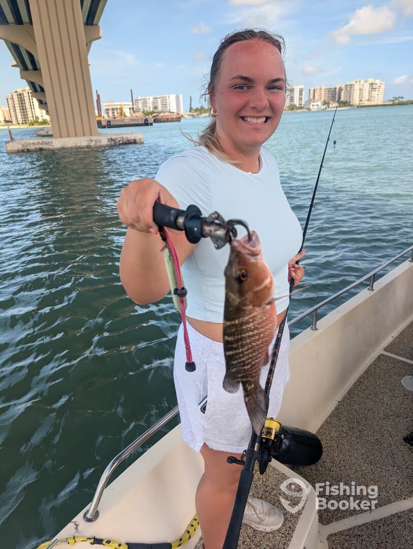 A young angler proudly displaying a freshly caught fish while fishing under a bridge in a coastal area.