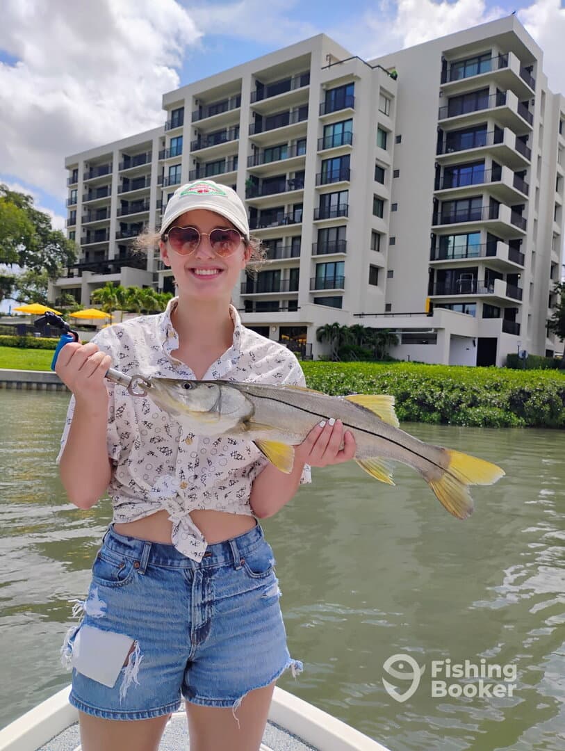 A young angler proudly displaying a Snook while fishing near a waterfront property.