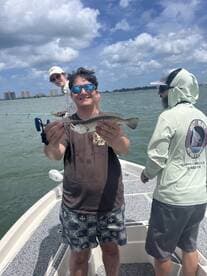 A young angler proudly displaying a Speckled Trout while fishing on a boat in a coastal environment.
