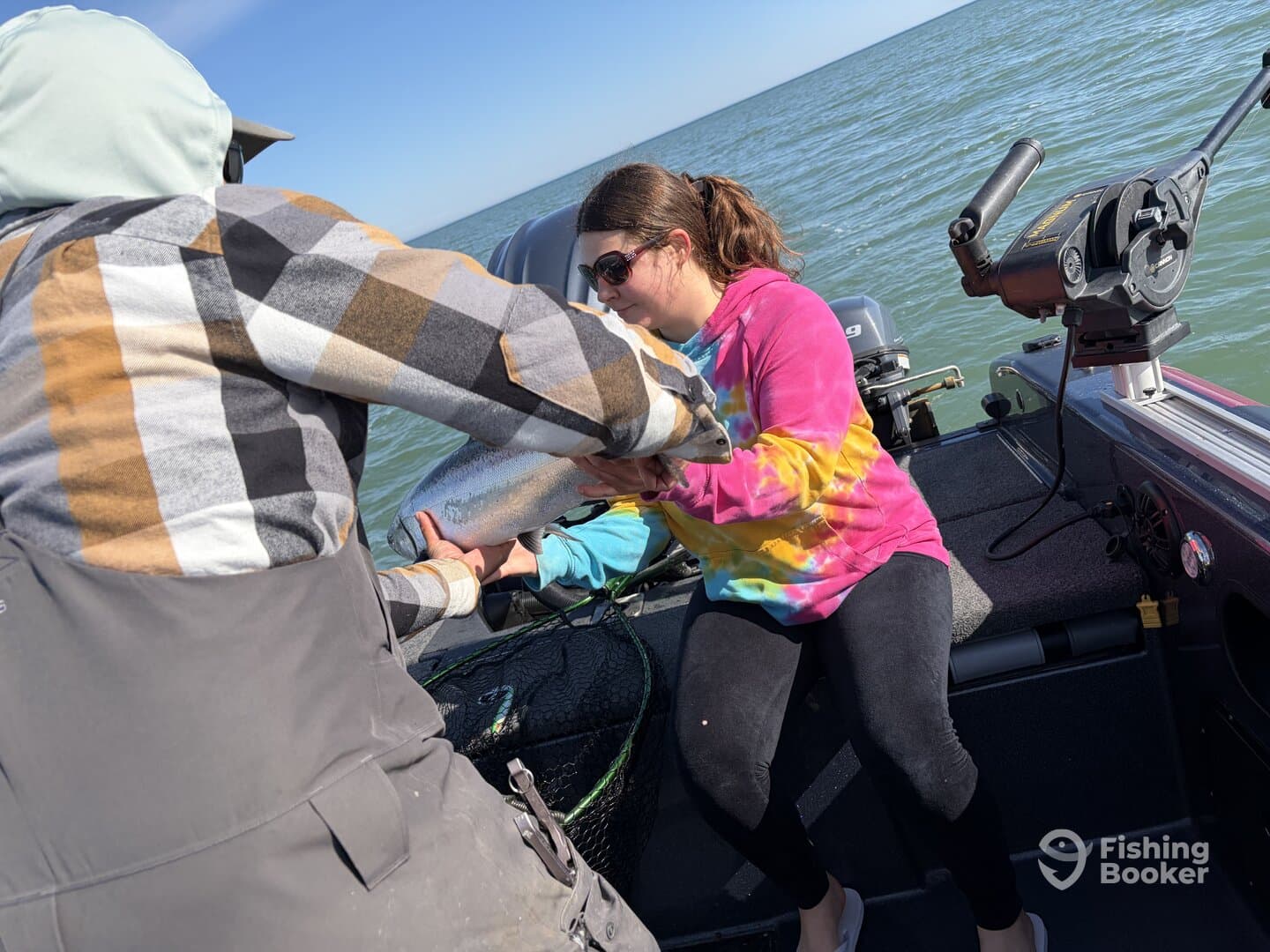 A young angler excitedly receives a large fish from a fellow fisherman while out on a boat, showcasing a memorable fishing experience.