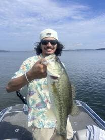 Angler proudly displaying a large Largemouth Bass while fishing on a lake, showcasing a vibrant summer outfit.