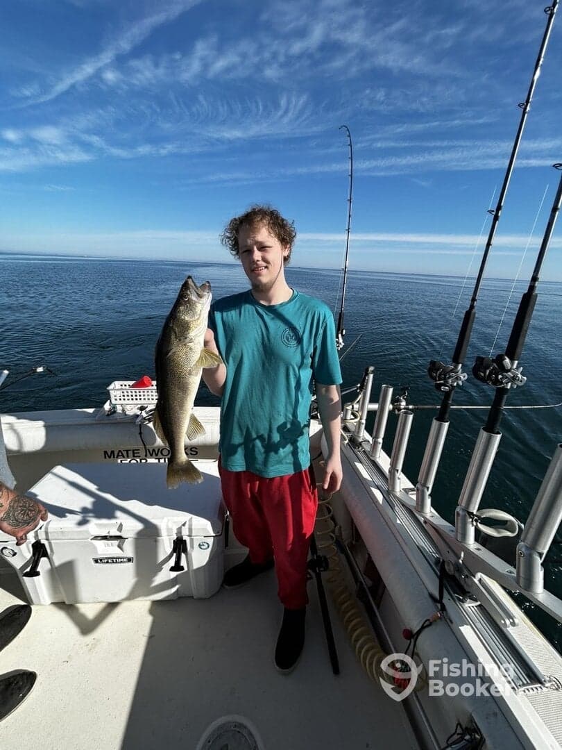 A young angler proudly holding a large Walleye while fishing on a boat, showcasing a successful catch in clear waters.