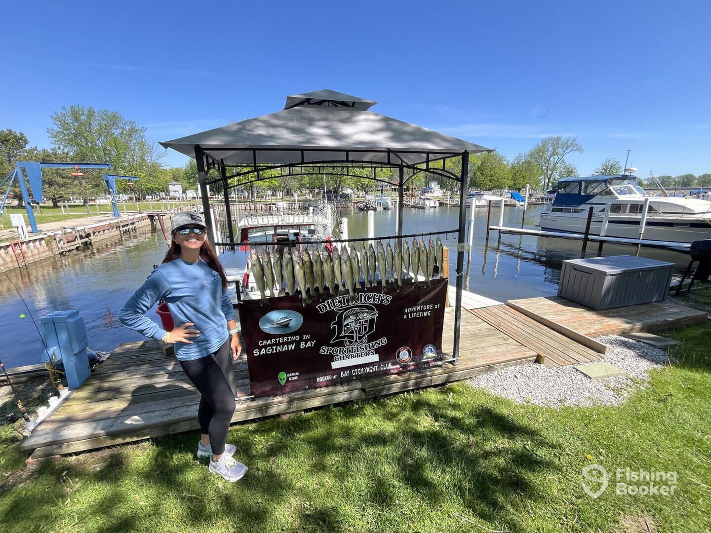 A smiling angler poses beside a catch board displaying multiple fish at a marina in Saginaw Bay, showcasing a successful fishing trip.