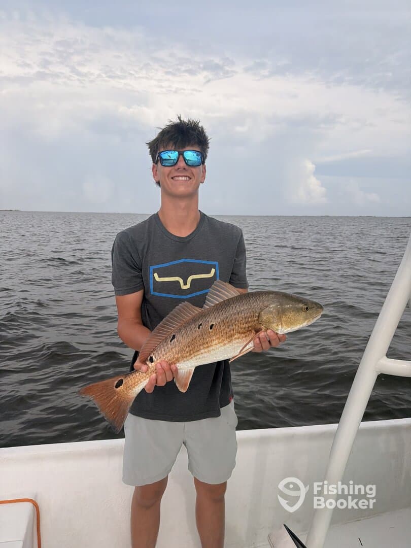 A young angler proudly displaying a Redfish while fishing on a boat, showcasing a successful day on the water.