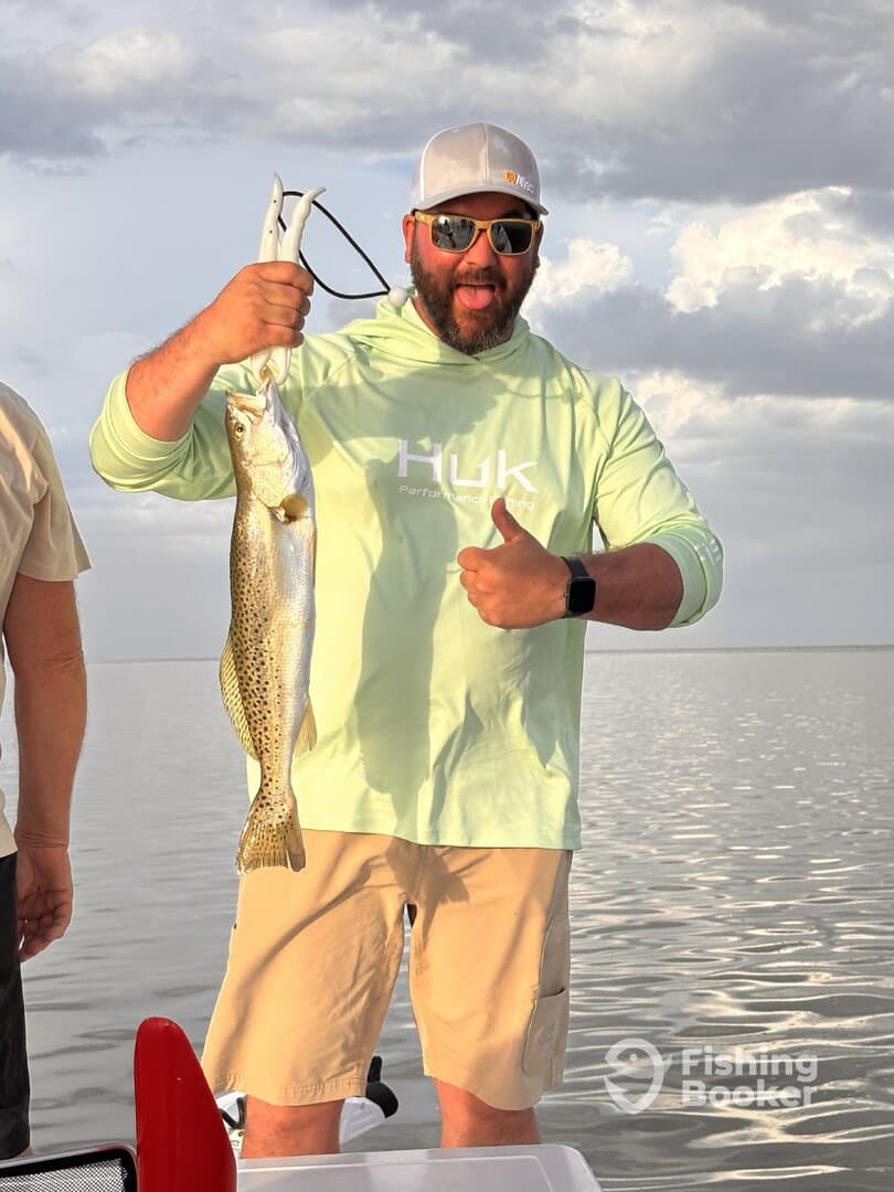 Angler proudly displaying a large Speckled Trout while enjoying a fishing trip on calm waters.