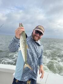 Angler proudly displaying a Spanish Mackerel while fishing on a boat, showcasing a successful day on the water.
