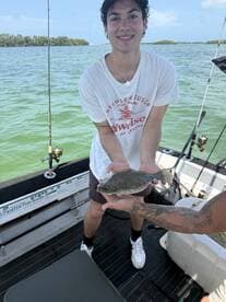 A young angler proudly displaying a Flounder while fishing on a boat in a scenic coastal environment.