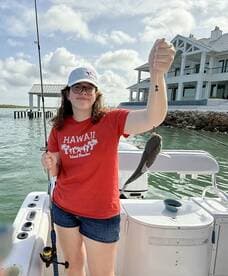 A young angler proudly displaying a fish while fishing from a boat in a scenic coastal setting.