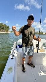 An angler proudly displaying a freshly caught fish while standing on a boat in a scenic fishing location.