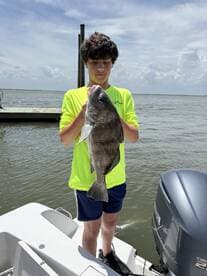 Young angler proudly holding a Black Drum while standing on a boat in a coastal fishing environment.