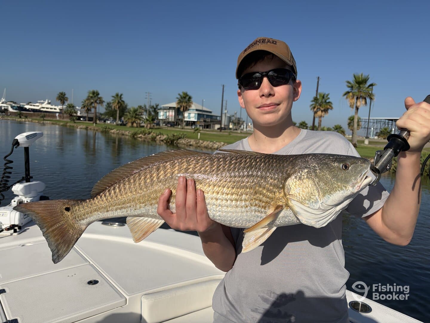 A young angler proudly displaying a large Redfish while fishing in a scenic coastal area.
