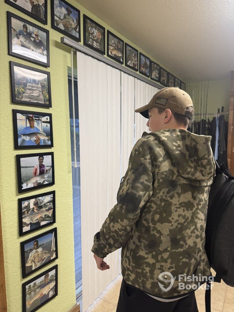A young angler is admiring a wall of fishing photos showcasing various catches, highlighting the fishing experiences shared with others.